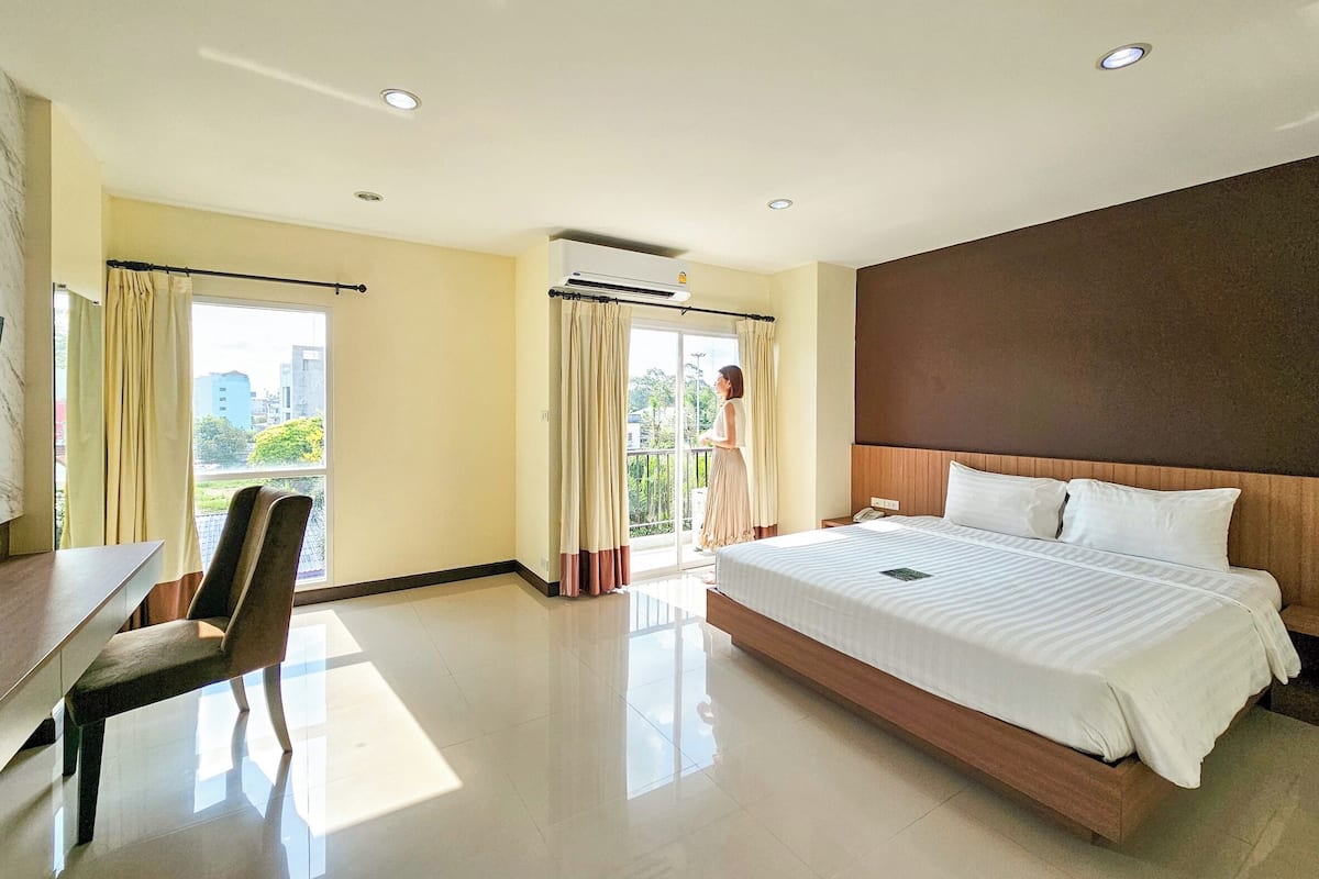 A hotel room with a bed, a desk, a chair, a balcony with curtains, and a city view.