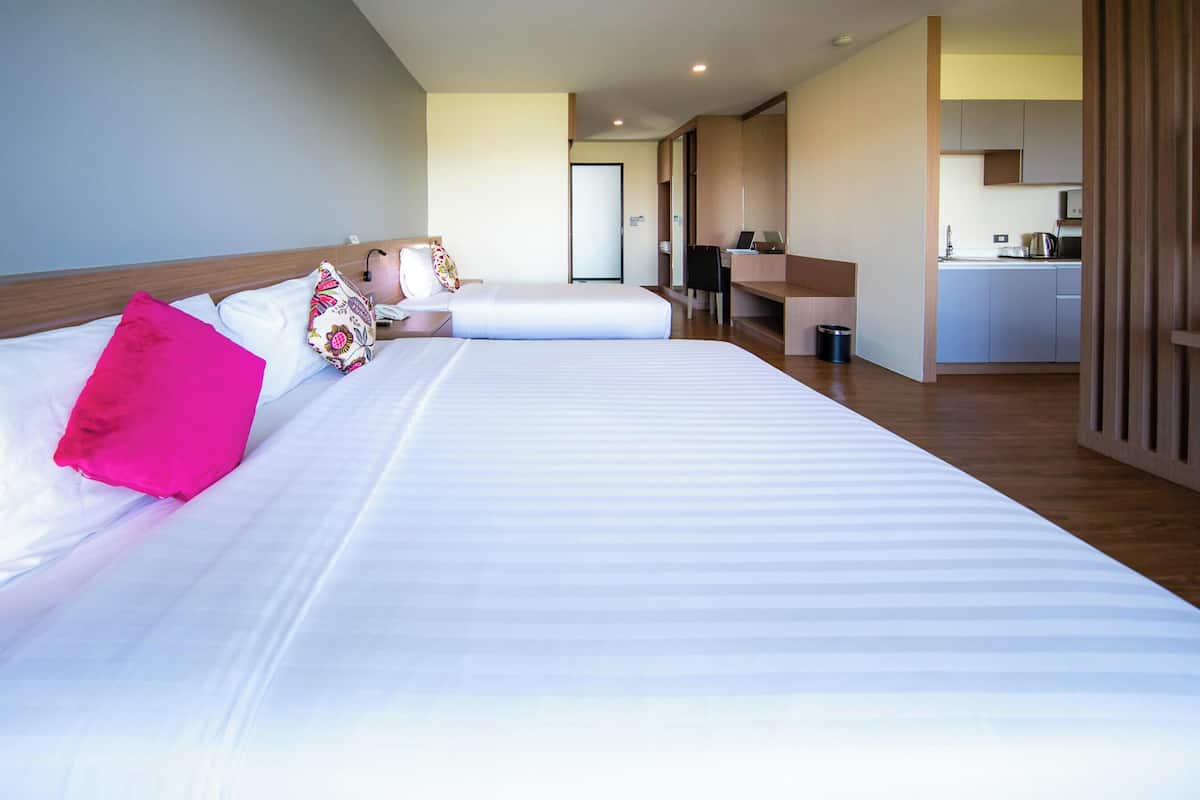 A hotel room with two beds, a kitchenette, and a bathroom.