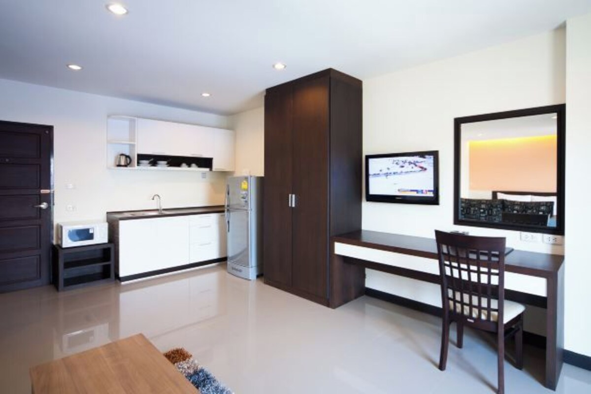 A modern kitchen with white cabinets, a dark wooden cabinet, a refrigerator, and a dining area with a table and chair.