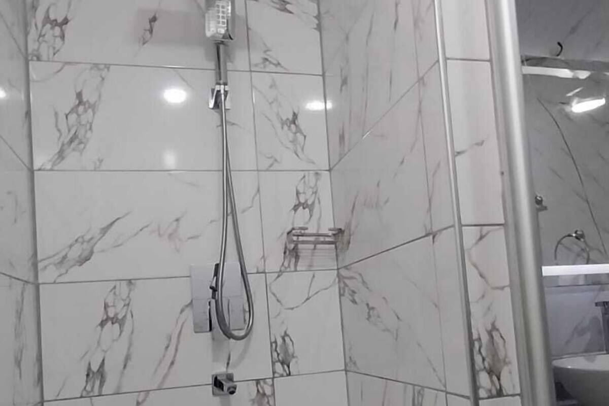 A shower area with a handheld showerhead, a wall-mounted control panel, and a floor drain.