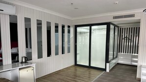 Habitación de hotel con piso de madera, armario blanco, pequeña kitchenette y puerta corrediza de vidrio que da a un balcón.