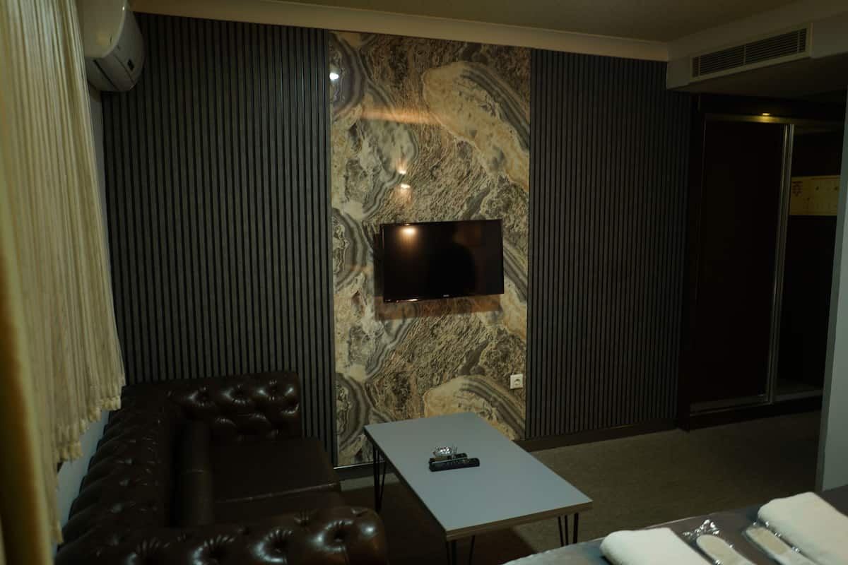A modern living room with a marble-patterned wall, a flat-screen TV mounted above a sofa, and a small table with a remote control.