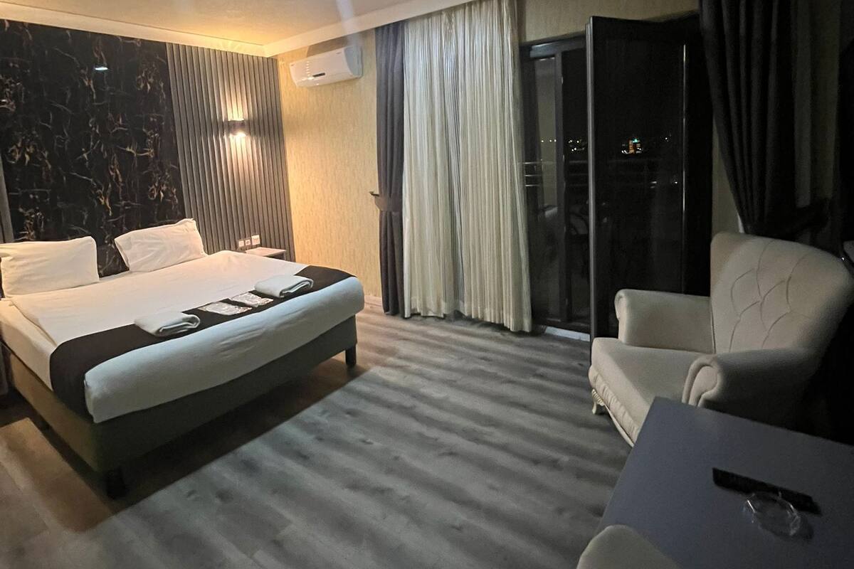 A modern hotel room with a large bed, a seating area, and a view of the city at night.
