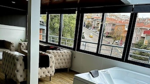 Un baño moderno con una bañera grande, piso de madera y vistas a la ciudad a través de amplios ventanales.