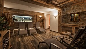 A rustic interior with wooden floors, stone walls, and a large painting of a mountain landscape. There are several chairs and a small table. - Hotel Mirabel (Marebbe)