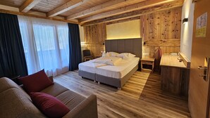 A wooden-paneled bedroom with a bed, bedside table, and a sofa. - Hotel Mirabel (Marebbe)