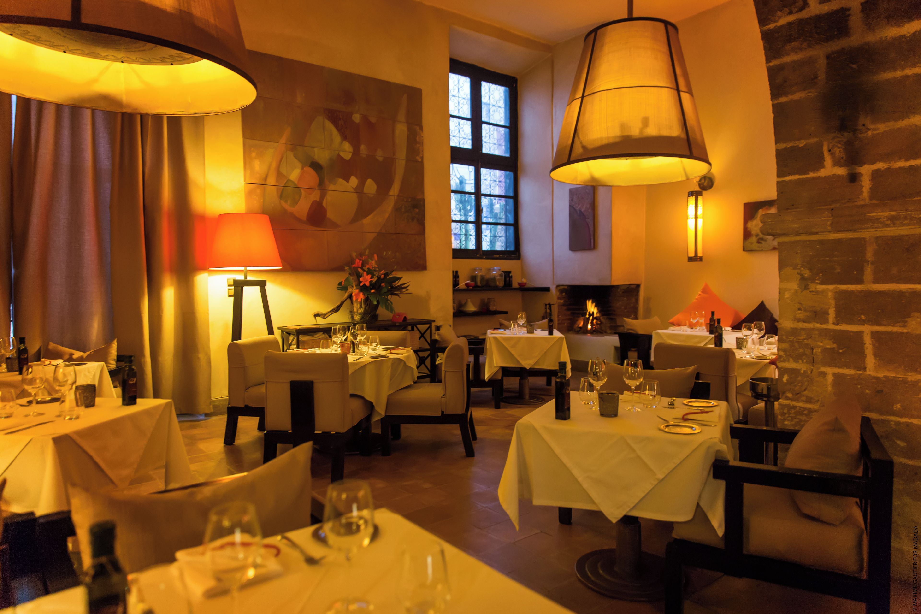A restaurant with multiple tables, candles, and a brick wall.