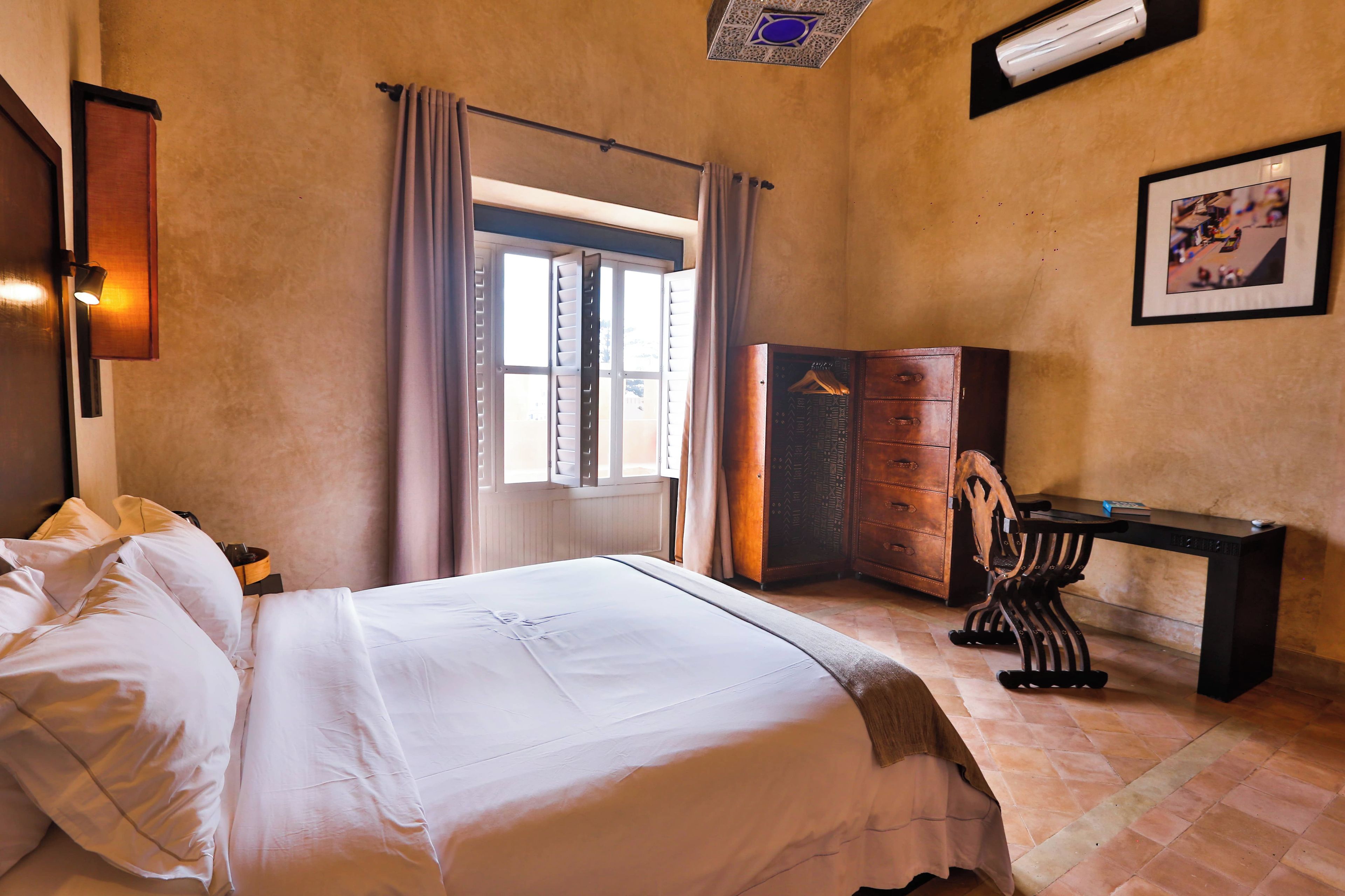 Une chambre d’hôtel avec un lit, une commode, un bureau et une fenêtre avec des rideaux.