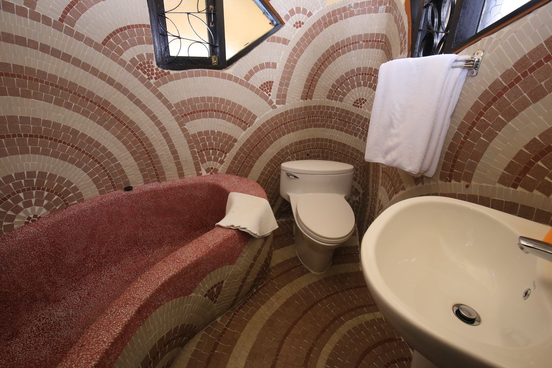 Un baño con piso de baldosas, inodoro blanco, lavamanos y un tapete de baño rojo.