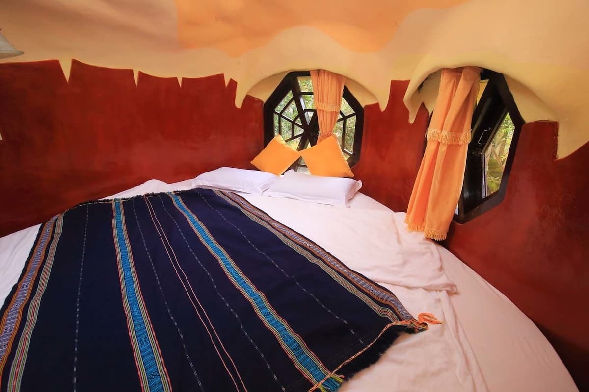 A bed with a striped blanket, two windows with curtains, and a unique ceiling design.