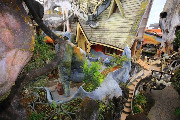 A whimsical garden with large rock formations, a small wooden building, and a winding path. - Crazy House (Xuan Huong - Da Lat)