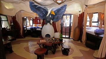 A room with a large bird sculpture, a dining table with chairs, and a bed with curtains.