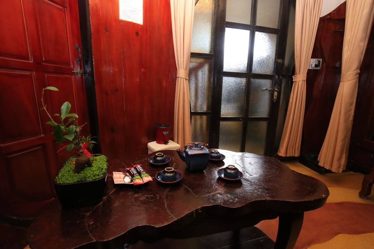 A traditional wooden table with teapots and a kettle, a potted plant, and a small table lamp.