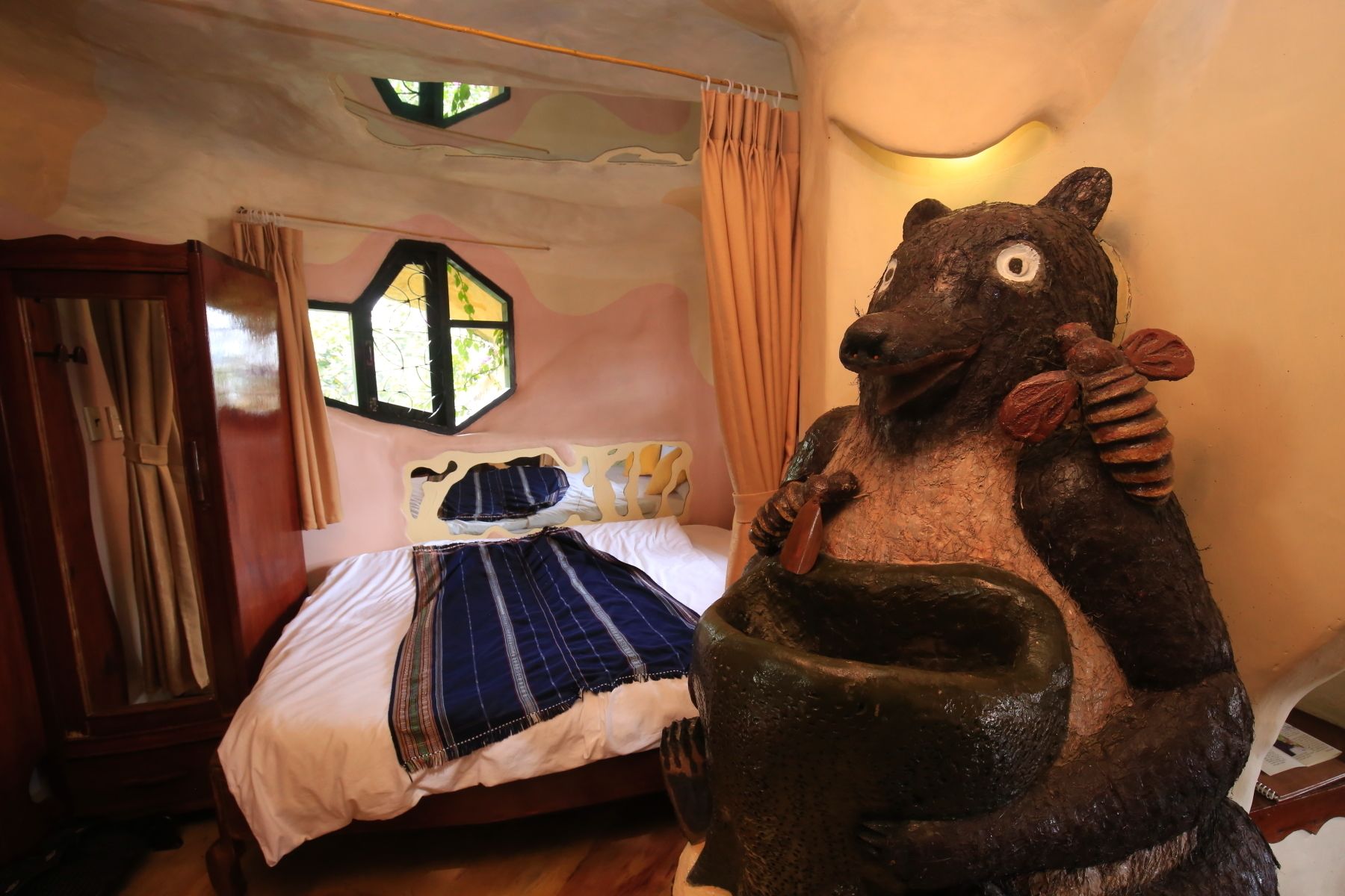A room with a bed, a window with curtains, and a bear sculpture.