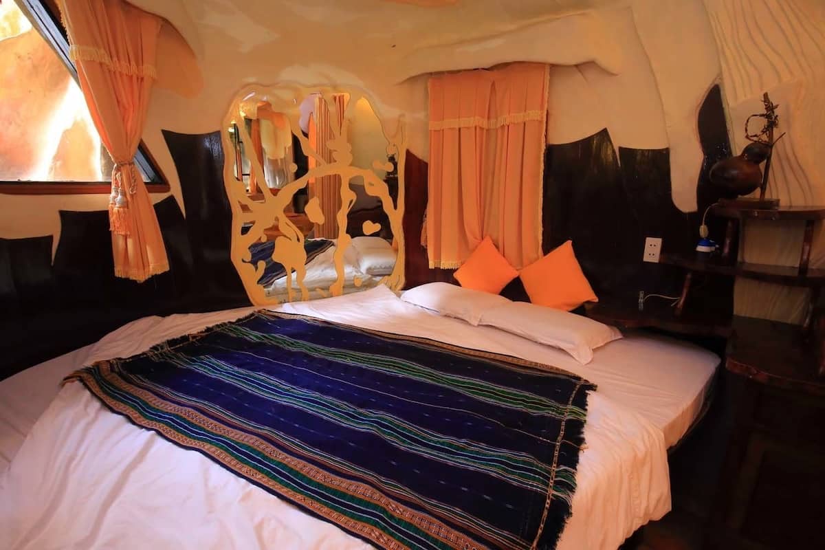 A bed with a patterned blanket, orange pillows, and a unique headboard design.