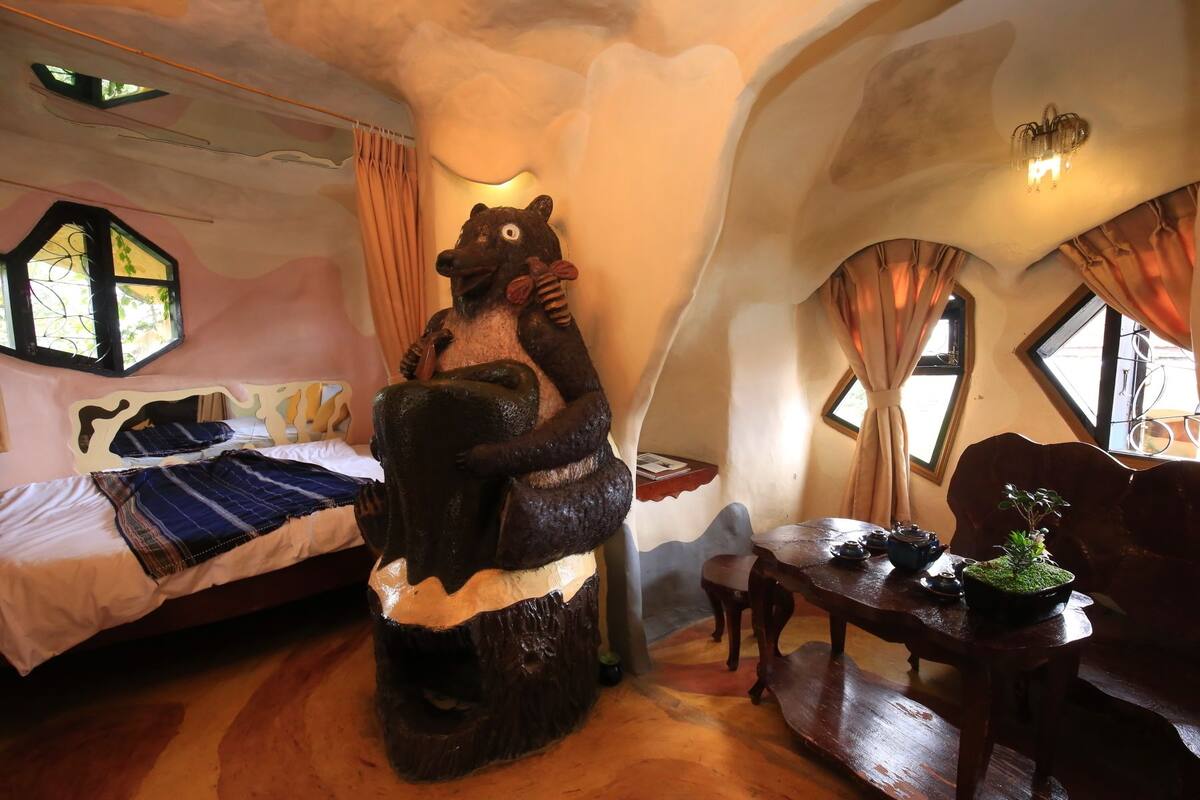 A room with a bed, a wooden table with a plant, and a bear sculpture.