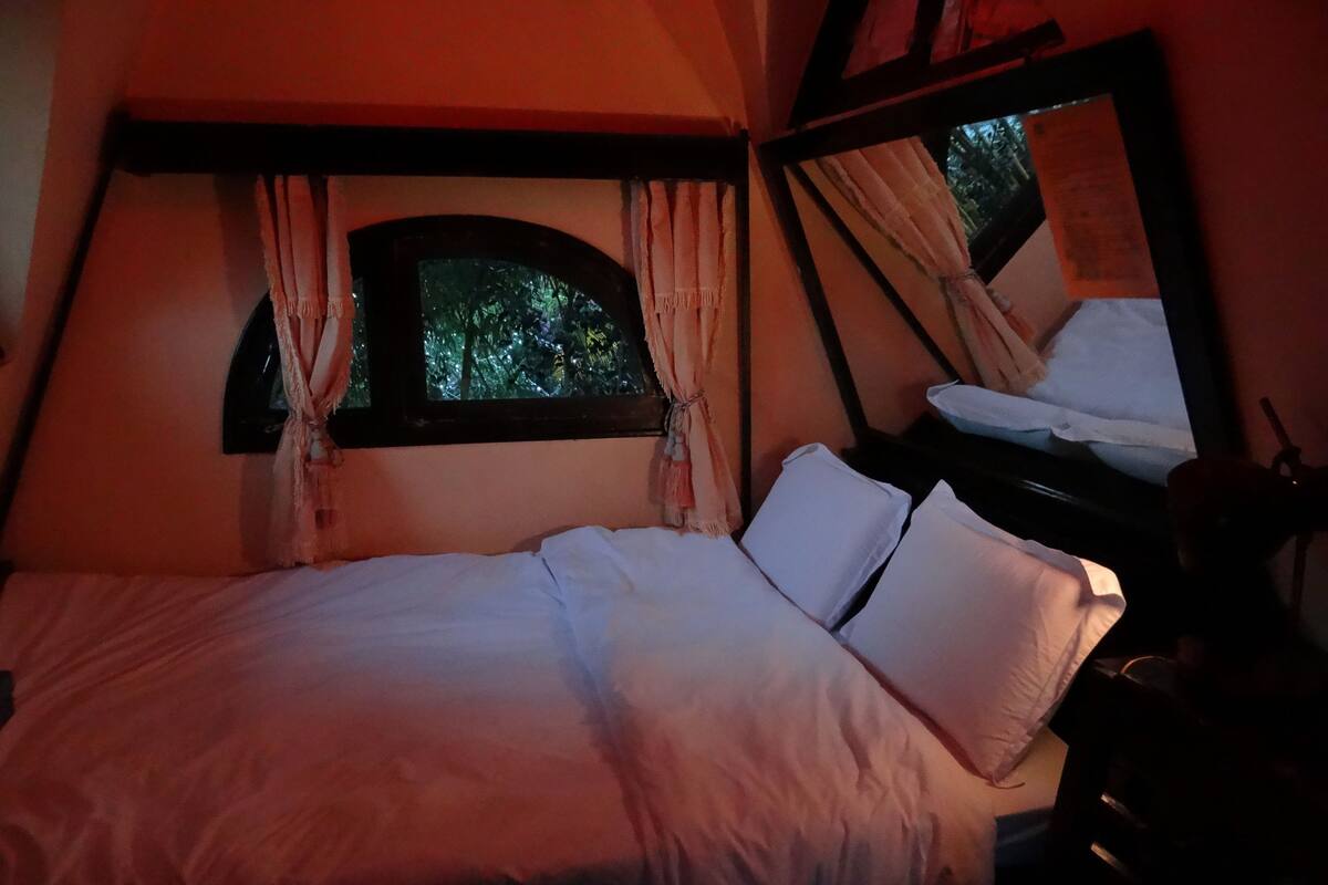 A bedroom with a bed, a window with curtains, and a mirror.