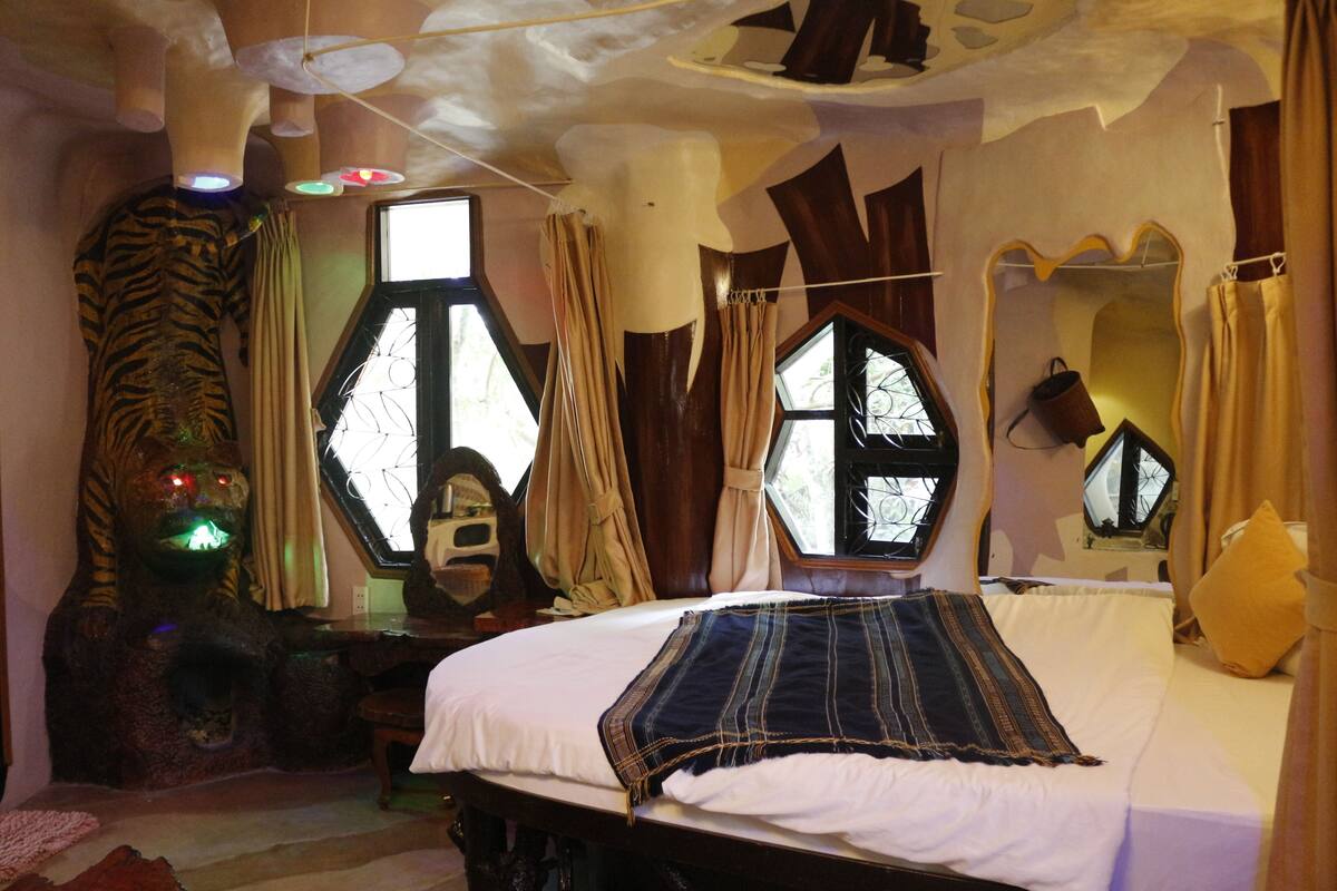 A room with a bed, a window with a geometric design, and a tiger statue.