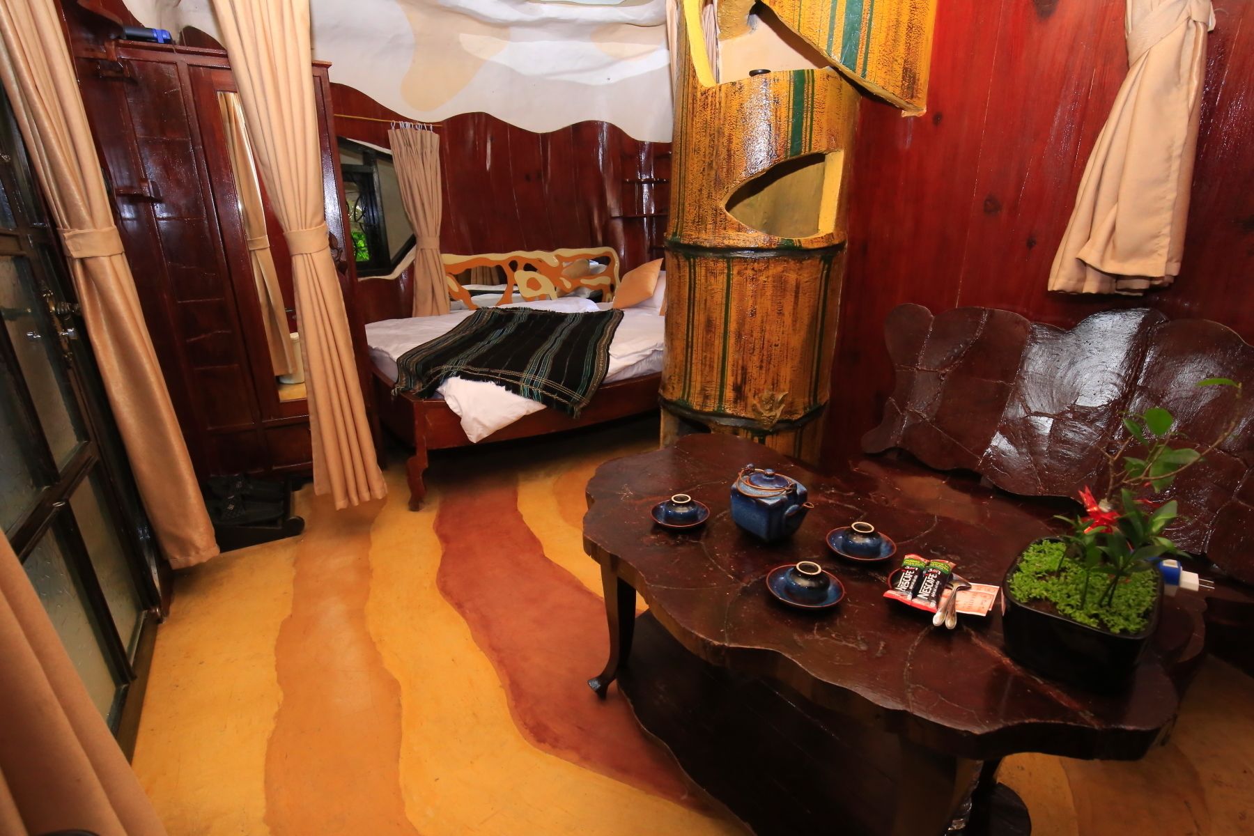 A cozy room with a bed, a wooden bench, a table with teapots, and a potted plant.