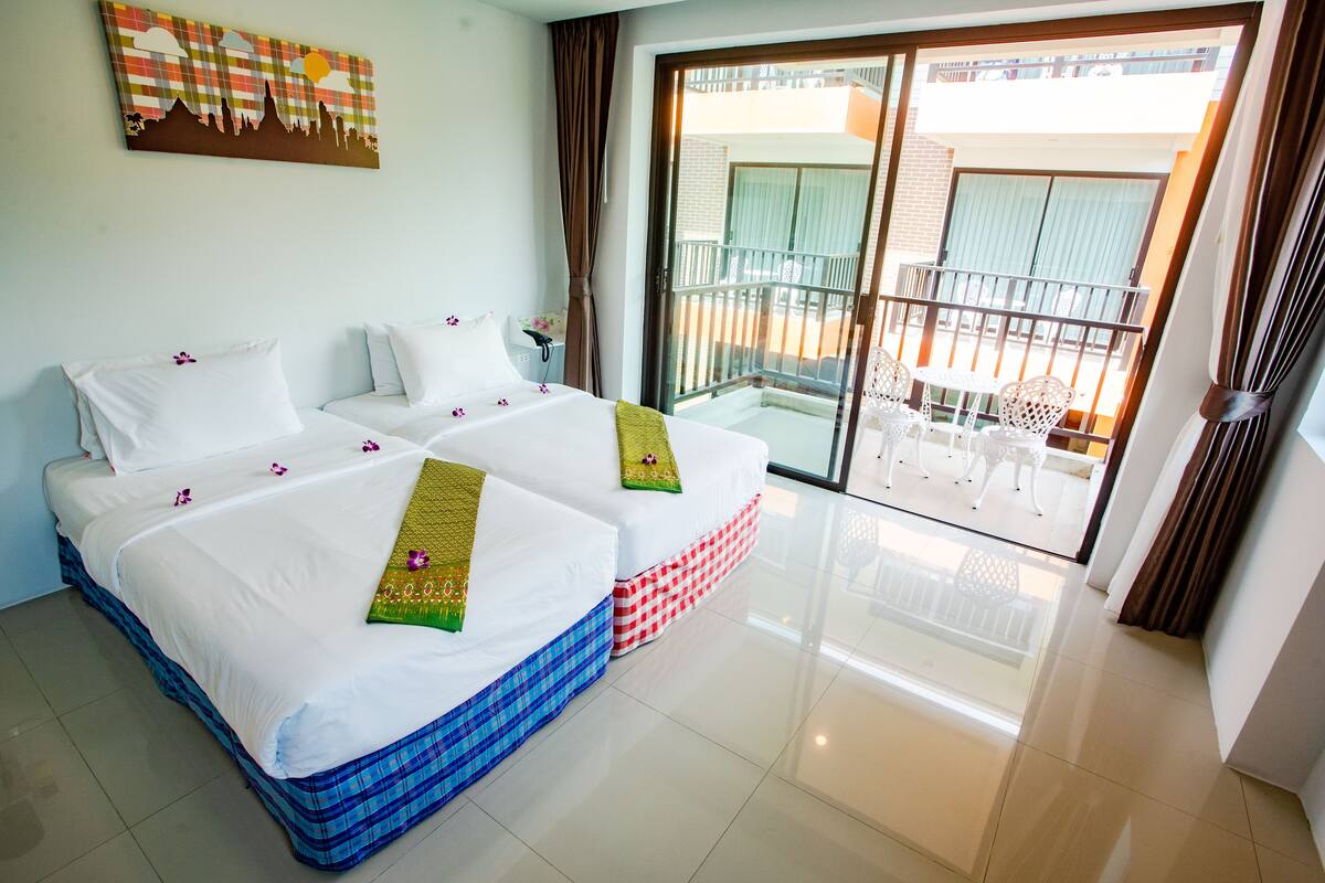 A hotel room with two beds, a balcony with a table and chairs, and a view of the outside.
