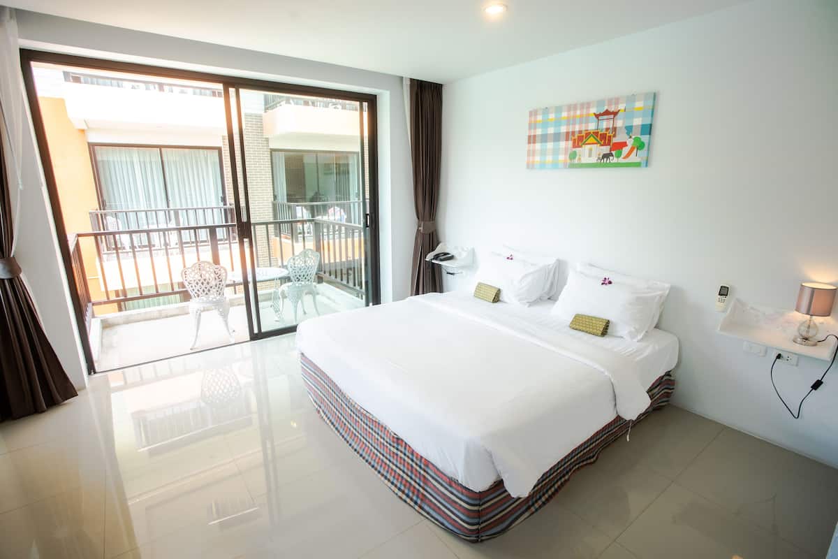 A hotel room with a large bed, a balcony with a chair, and a wall-mounted phone.