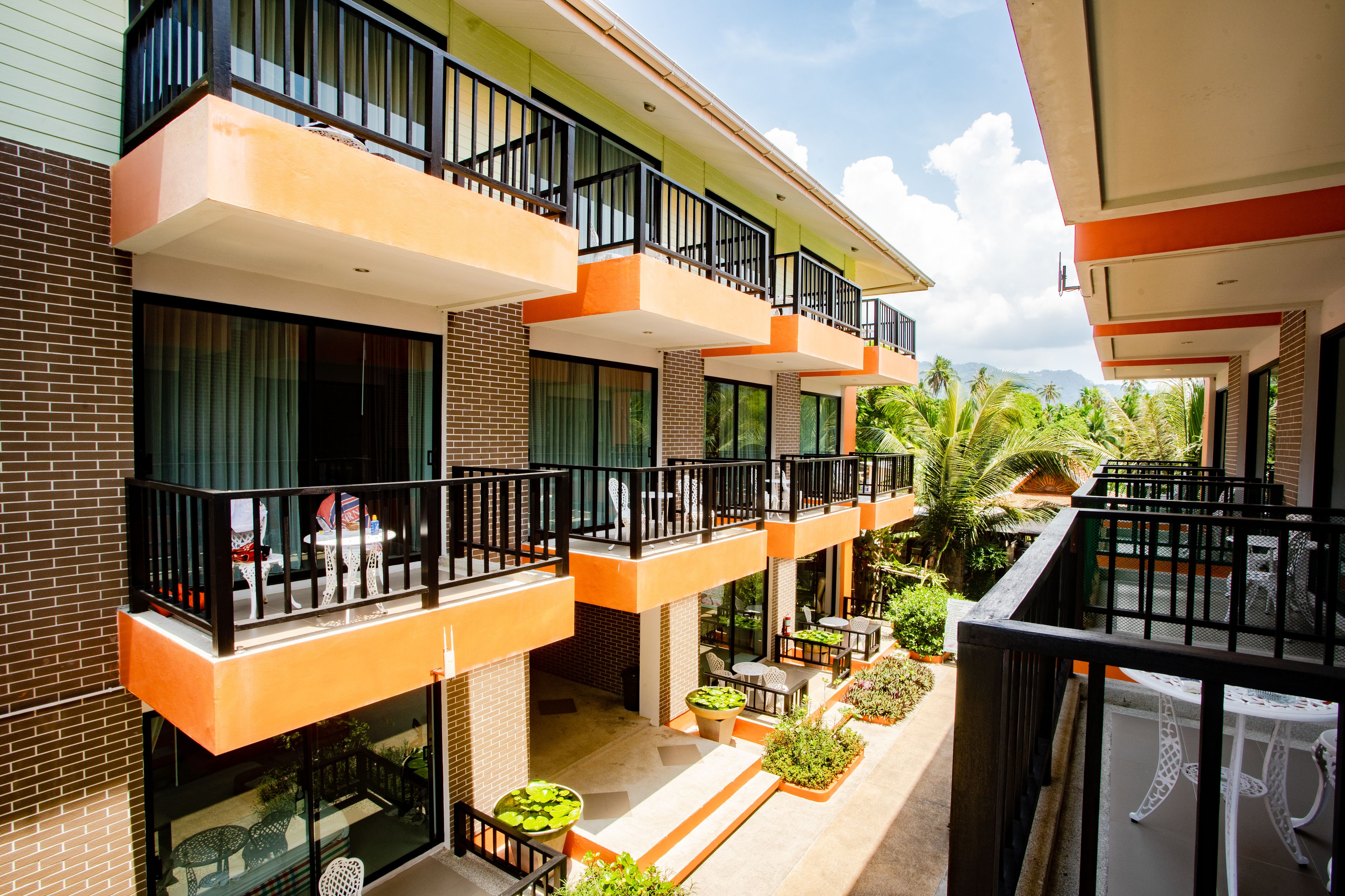 A multi-story hotel with balconies, outdoor seating, and potted plants.