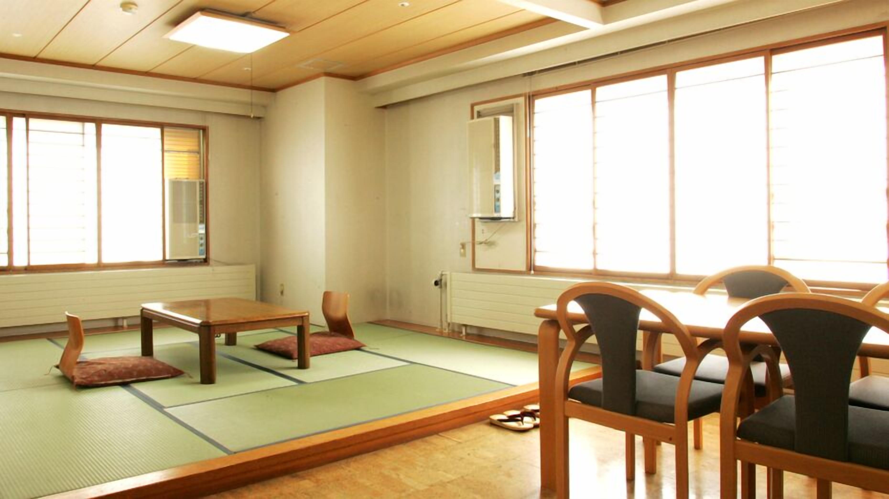A room with tatami mats, a wooden table, chairs, a radiator, and large windows.