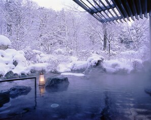 Un área tranquila de aguas termales, con árboles cubiertos de nieve y un farol de piedra.
