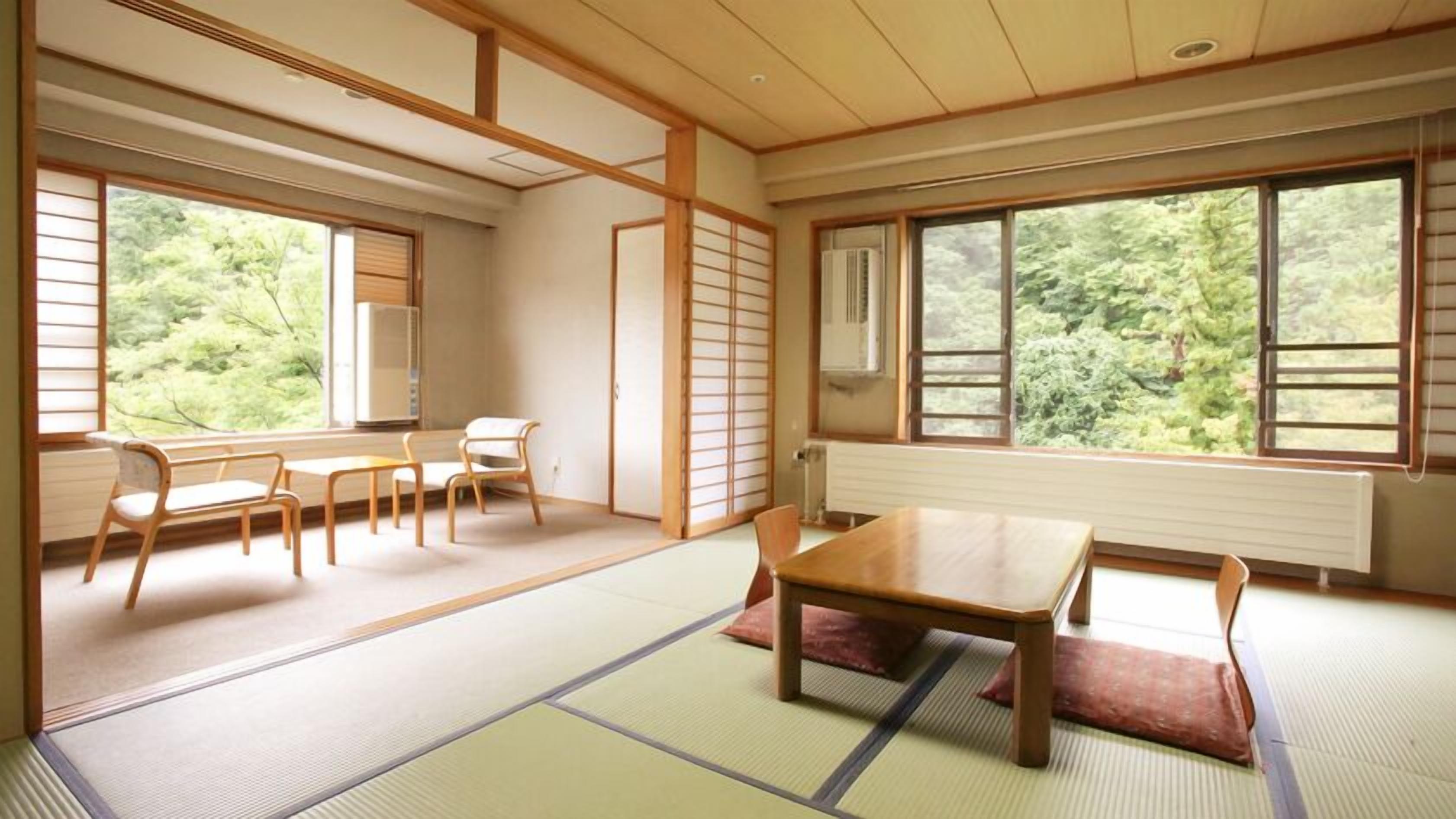 A traditional Japanese room with tatami flooring, a low table, chairs, and large windows with a view of greenery.