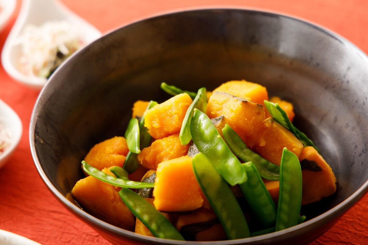 A bowl of food with chunks of orange and green vegetables.