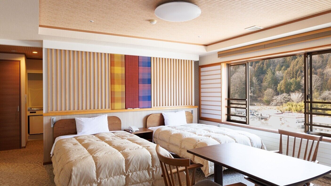 A hotel room with two beds, a dining table, a view of the outdoors, and a large window.