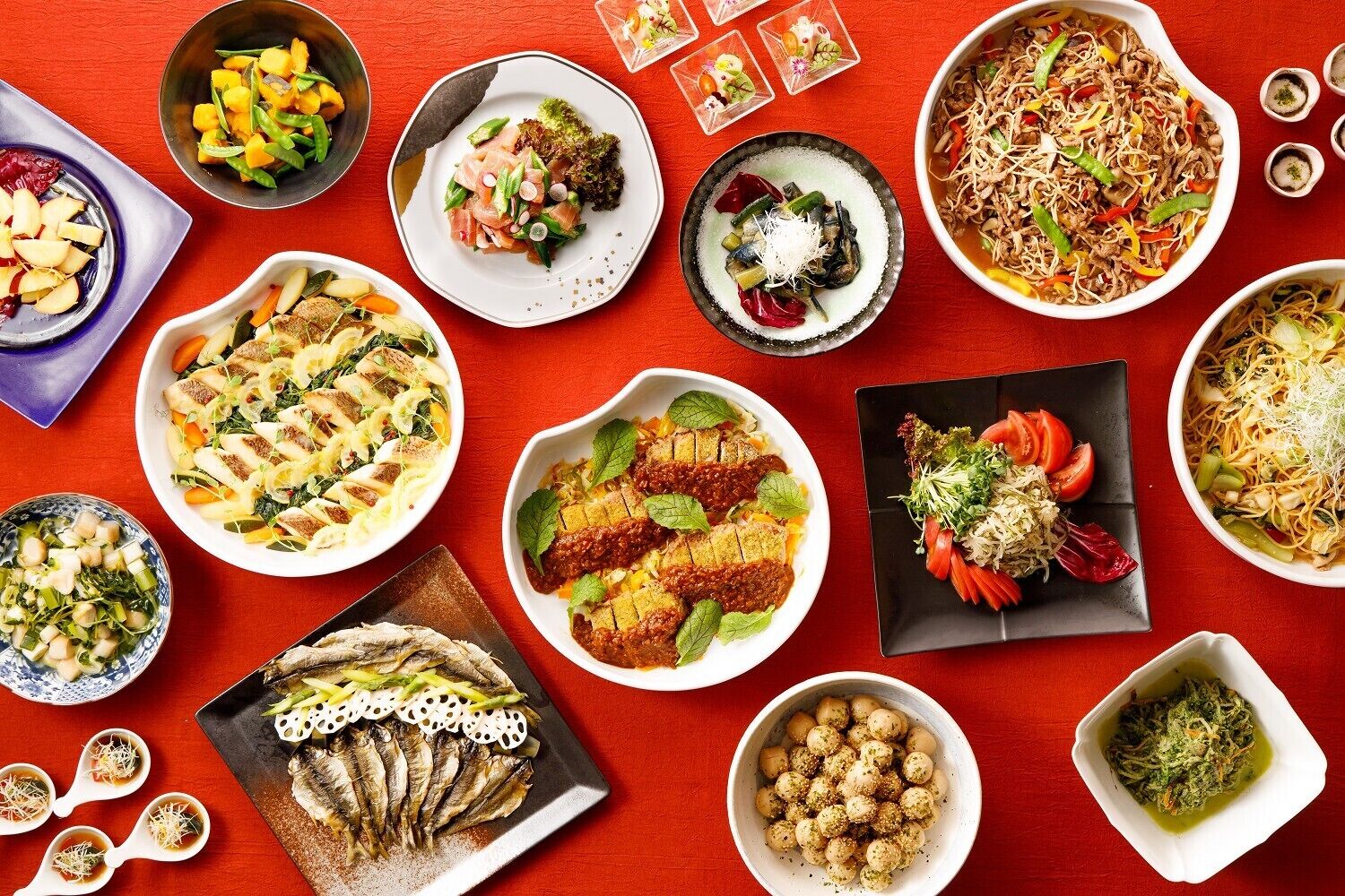 A variety of dishes arranged on a red tablecloth.