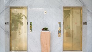 A lobby with marble flooring, two elevators with glass doors, and a wooden planter with a small plant. - Riverview Suites Taipei (Taipei)