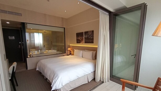 A modern hotel room with a large bed, a sitting area with a chair, a glass shower enclosure, and a large mirror. - Riverview Suites Taipei (Taipei)