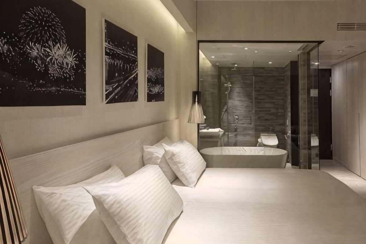 A modern bedroom with a large bed, a glass shower enclosure, and artwork on the walls.