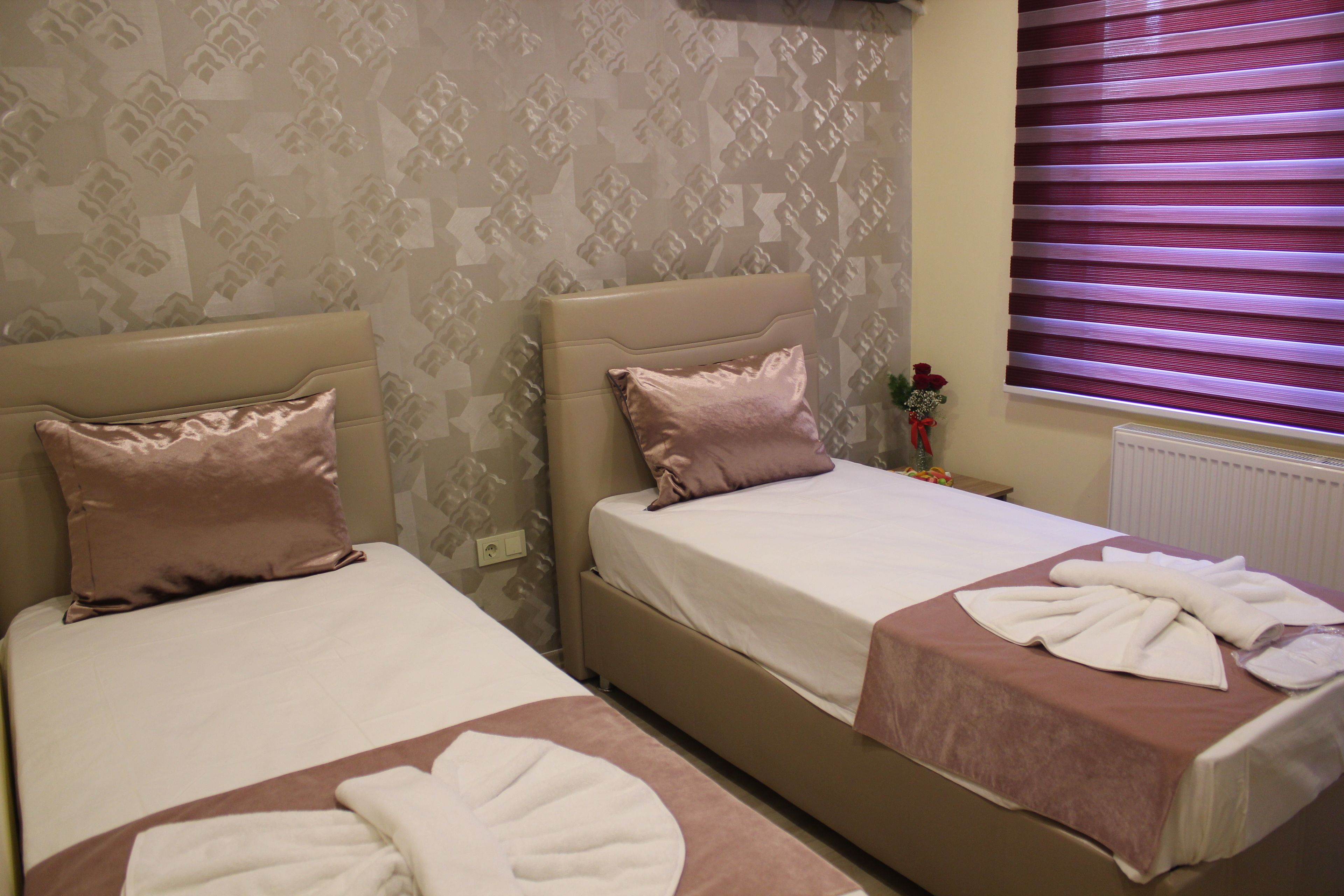 Two single beds with headboards, a window with blinds, and a patterned wallpaper.