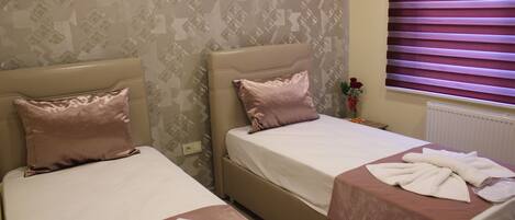 Two single beds with headboards, a window with blinds, and a patterned wallpaper.