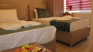 A hotel room with two beds, a wooden table with a fruit platter, and a window with blinds. - Görür Hotel (Istanbul)