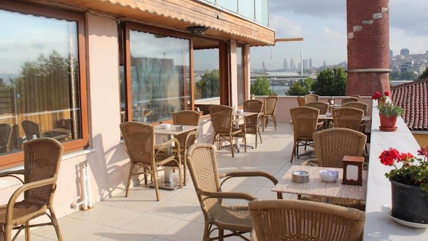 A rooftop terrace with wicker furniture, large windows, and a view of a city skyline. - Görür Hotel (Istanbul)