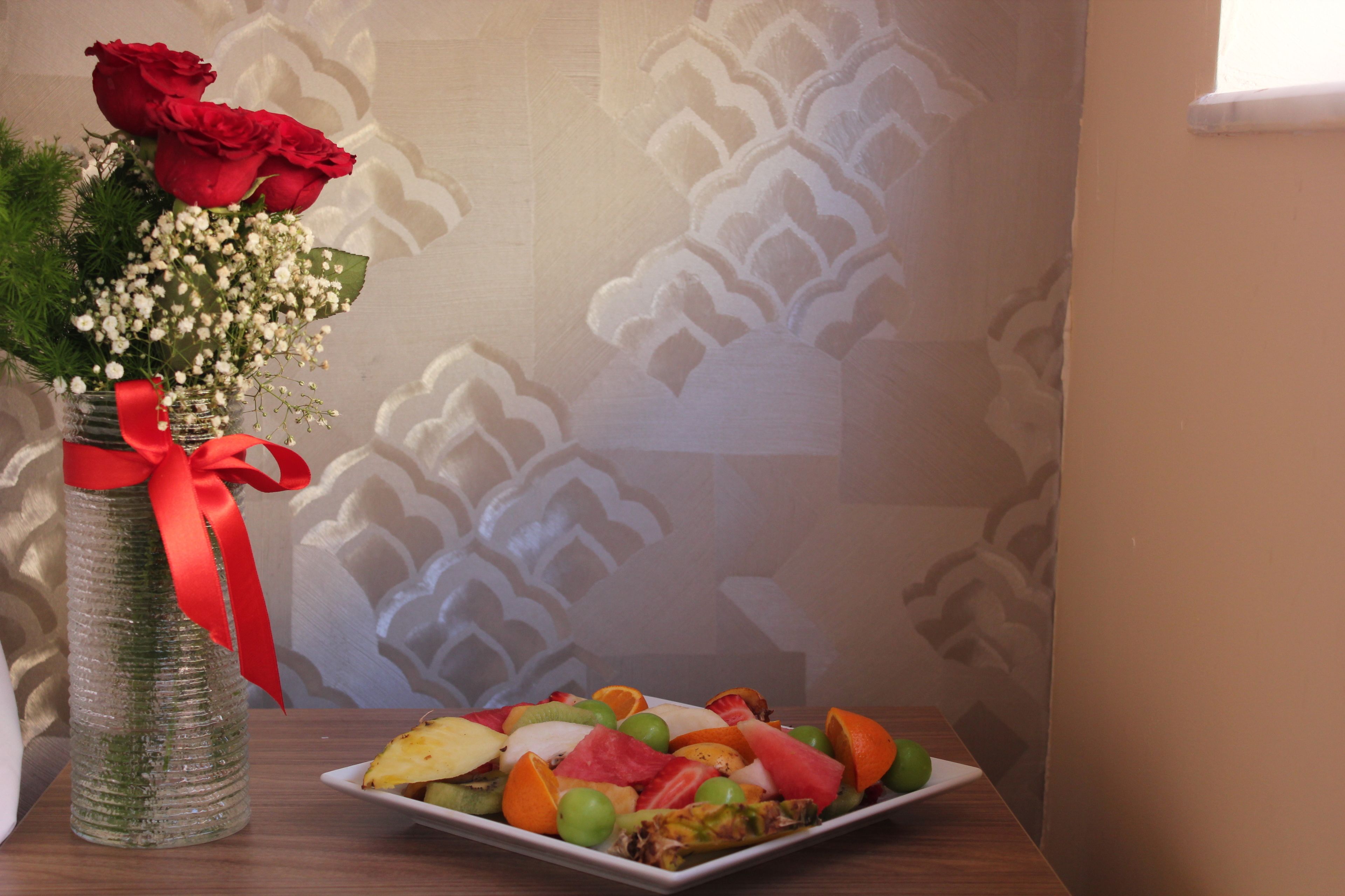 A table with a fruit platter and a vase with red roses.