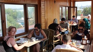 A dining area with wooden walls and large windows, tables with chairs, and people eating. - Görür Hotel (Istanbul)