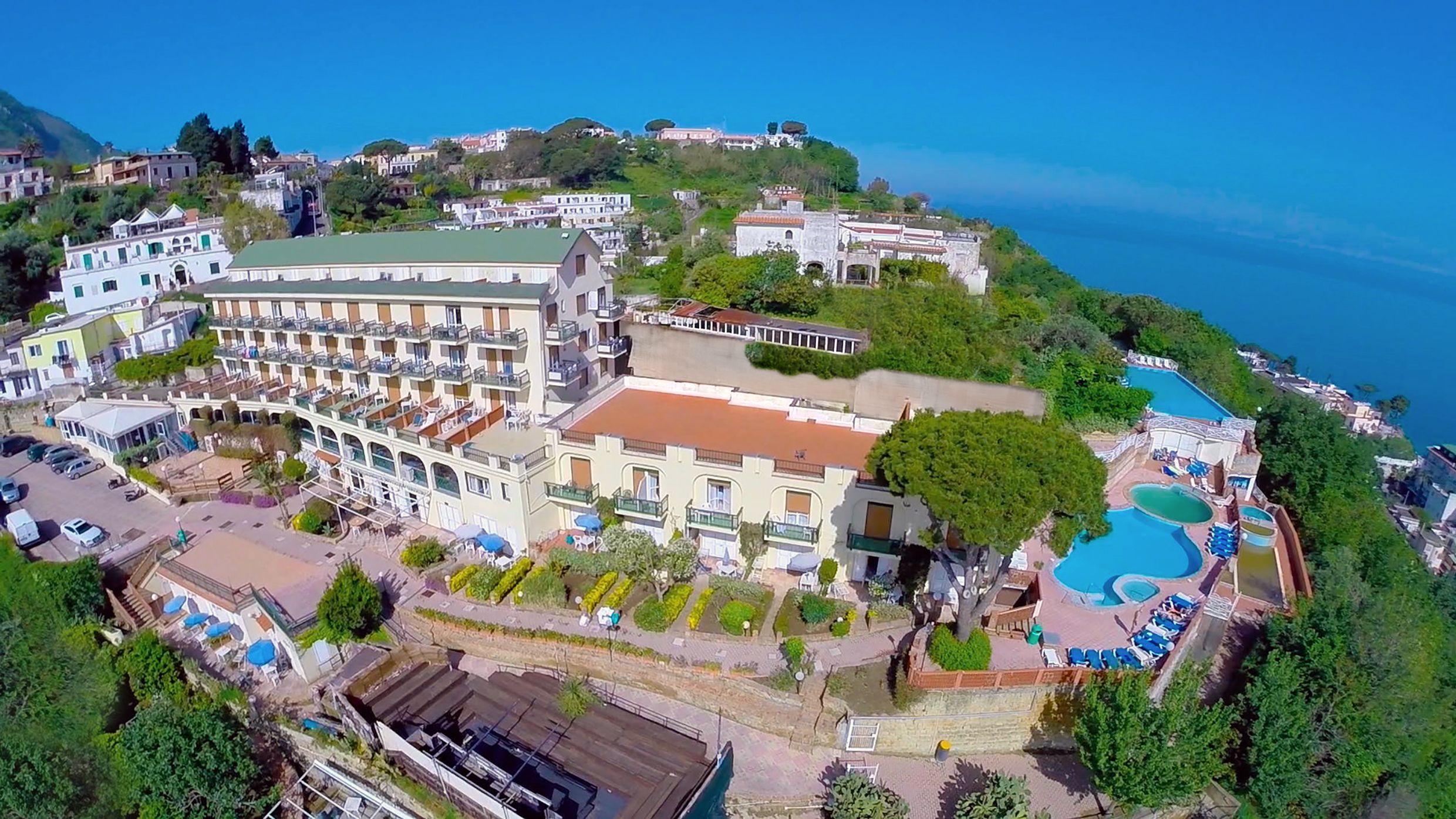 A coastal hotel with multiple balconies, a swimming pool, and lush greenery.