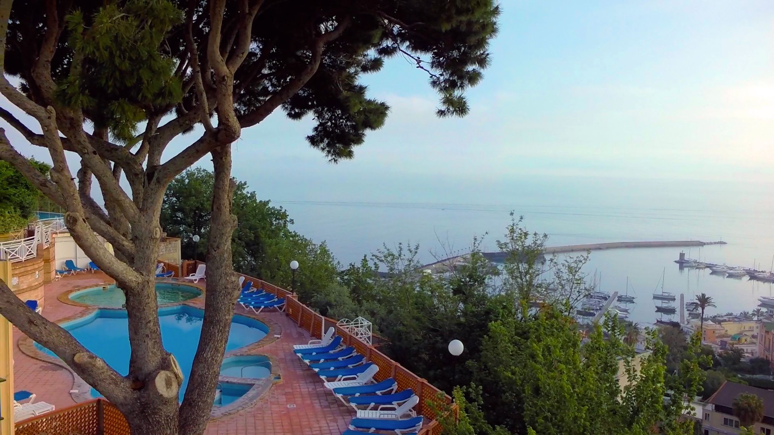 A pool area with multiple sun loungers and a view of the sea and marina.