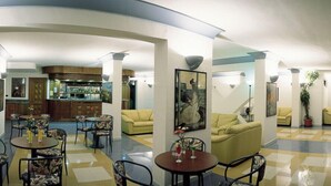Een hotellobby met een bar in het midden, meerdere zithoeken en een receptiebalie.