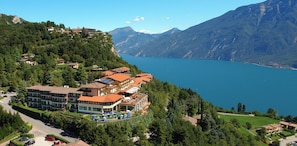 A hotel with multiple floors, a swimming pool, and a view of a lake and mountains. - Hotel Pineta Campi (Tremosine)
