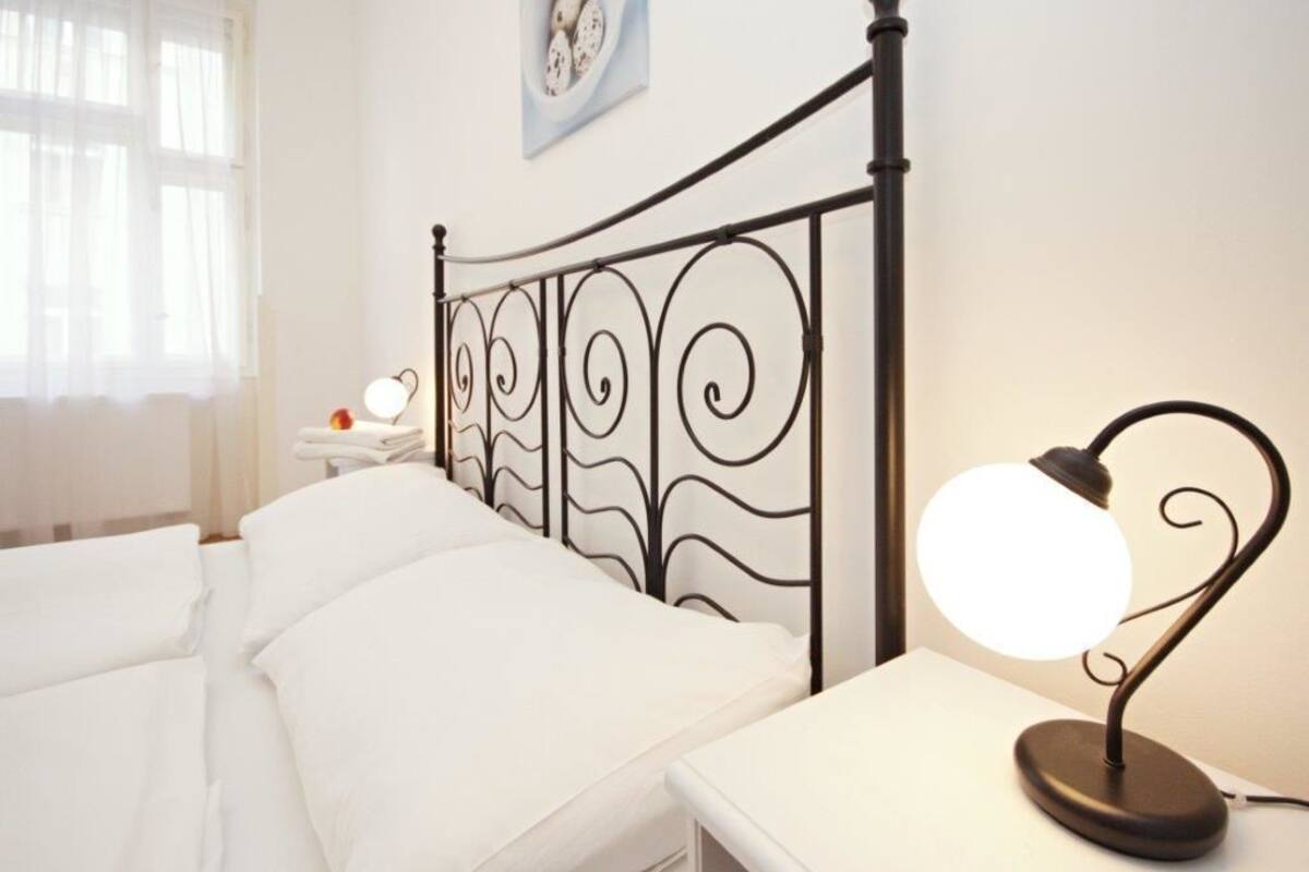 Cama bem arrumada com lençóis brancos, mesa de cabeceira com abajur e um quadro na parede com imagens de ovos.