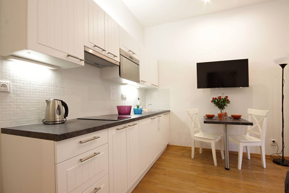 Uma cozinha moderna com armários brancos, bancada preta e um espaço de refeições com mesa e cadeiras.