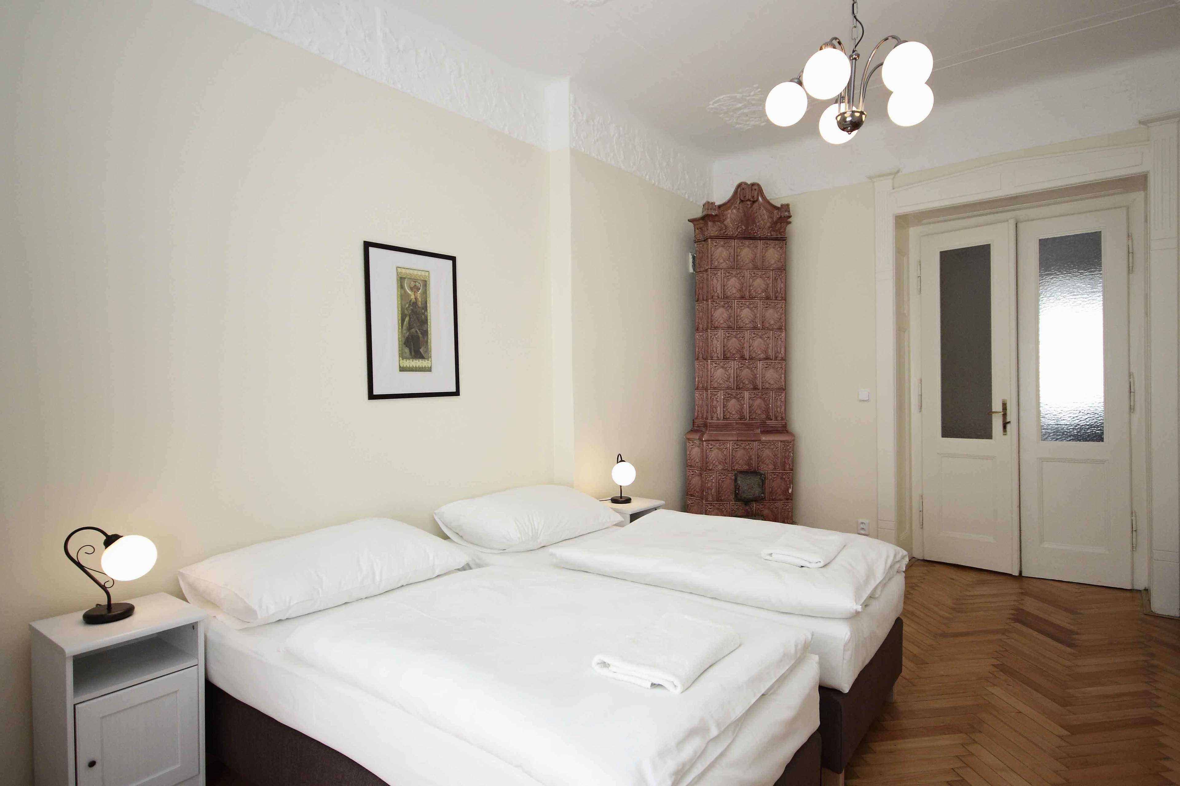 A hotel room with two beds, a nightstand with a lamp, a wooden cabinet, and a door with frosted glass panels.