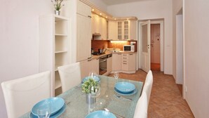 A compact kitchen with white cabinets, a microwave, and a sink. There is a dining table set with blue plates and wine glasses. - Prague Central Exclusive Apartments (Prague)
