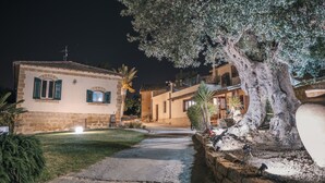 Un edificio de piedra con techo de tejas, un camino empedrado y un gran árbol de follaje denso.